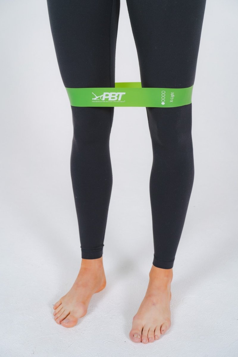 Dancer standing with green mini-loop band above knees for activation exercise